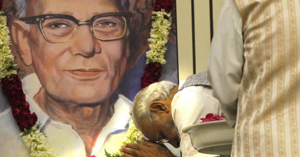 Photograph of a person bowing before a large garlanded painted portrait of Jaya Prakash Narayan